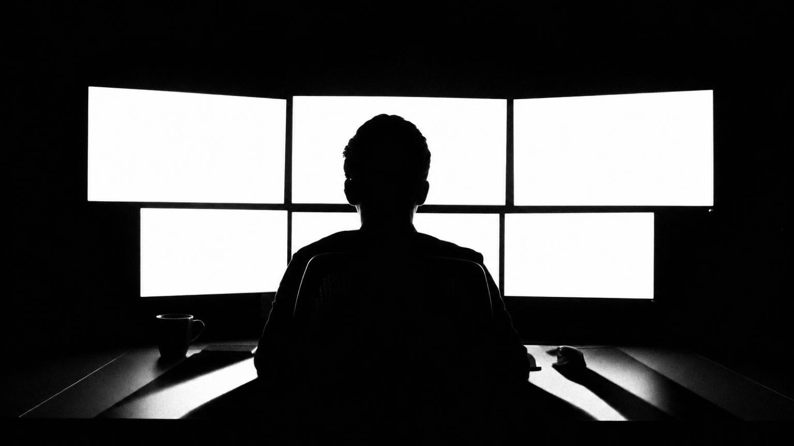 An engineer silhouetted in front of a bank of four monitors