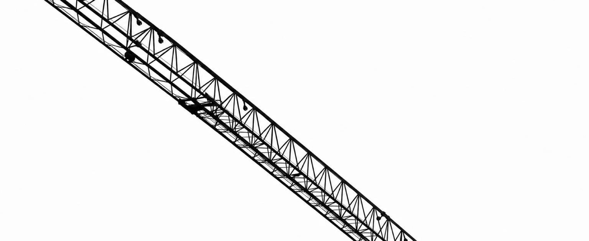 The lattice jib of a tower crane against a bright sky