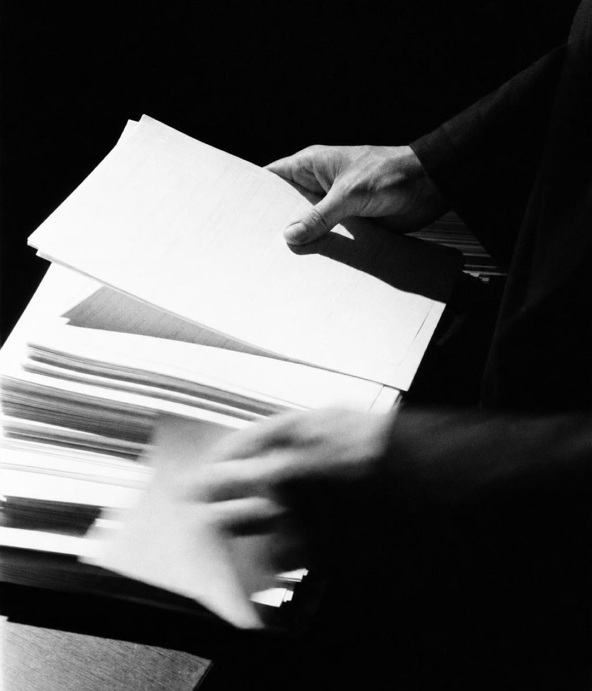 Hands working down through a deep stack of paper