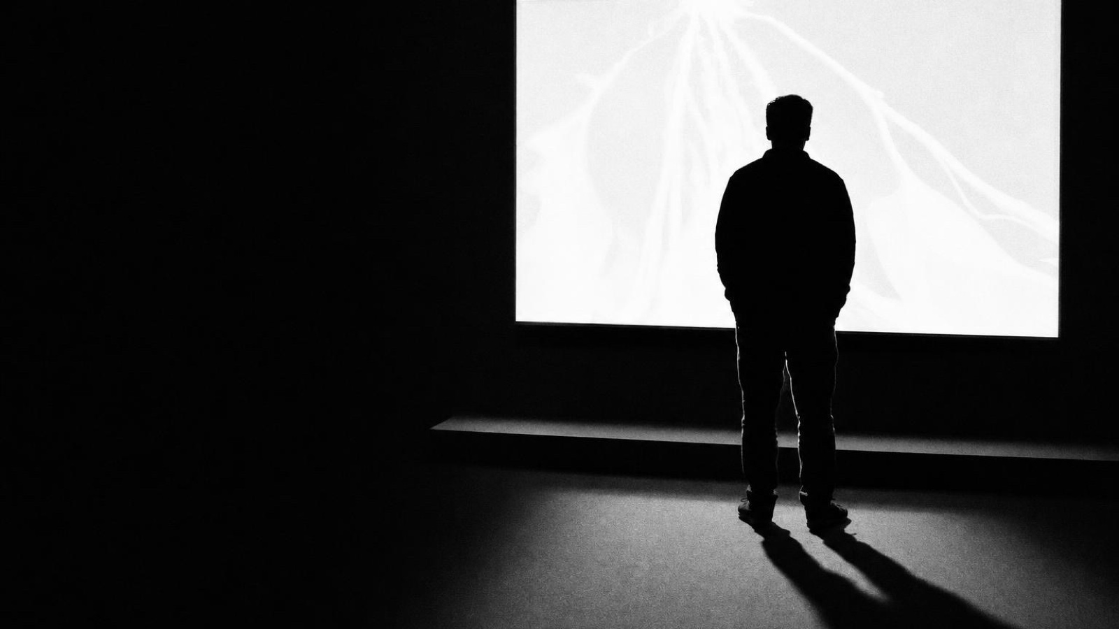 Someone standing in front of a lit projection screen in a dark room