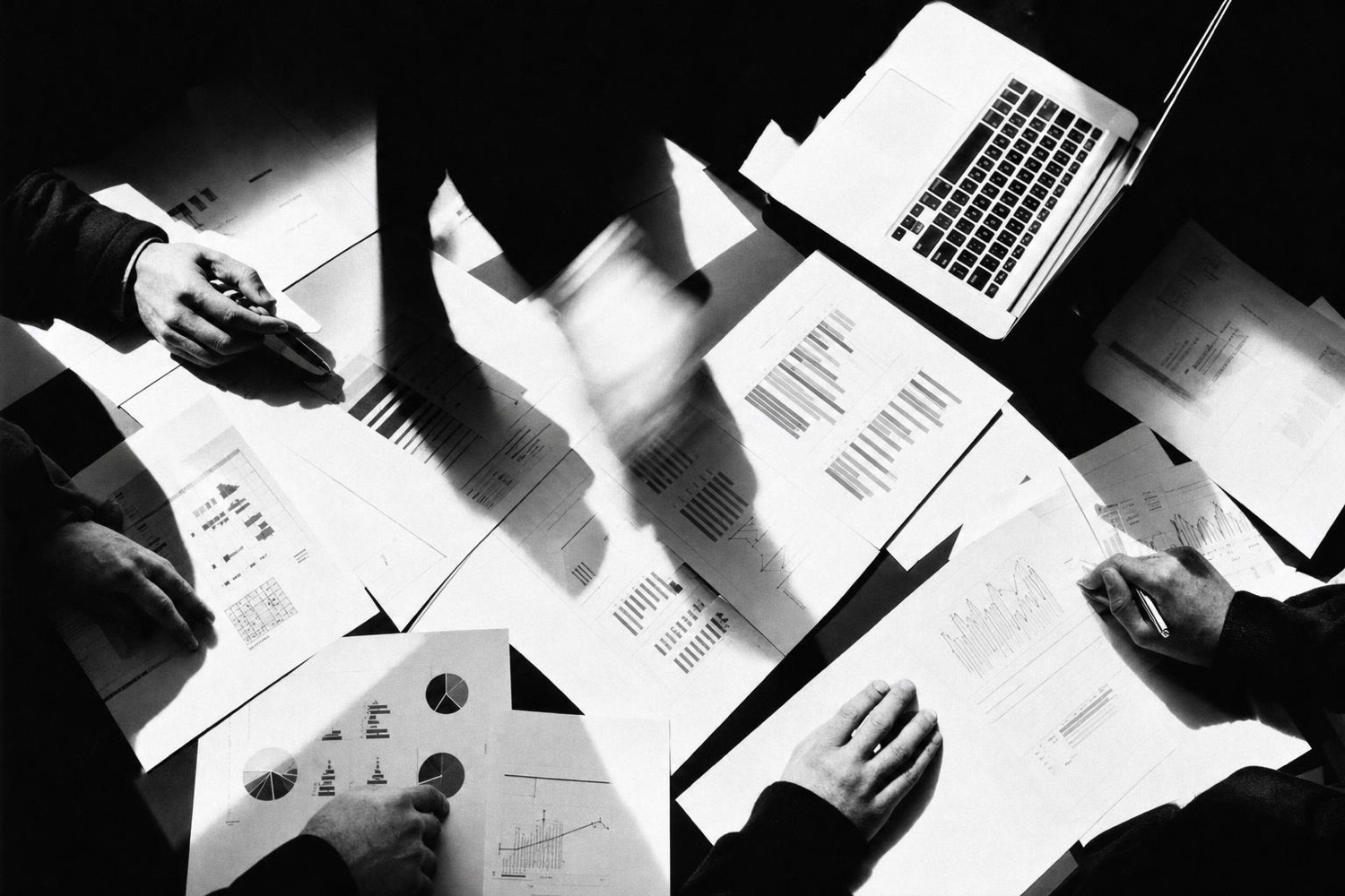 Hands, papers and laptops across a shared table, seen from above